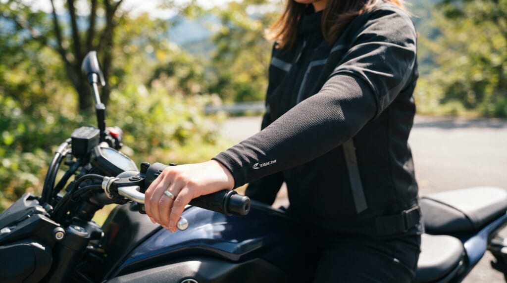 バイクにまたがったライダーが黒い冷感アームカバーを腕に装着している屋外の様子